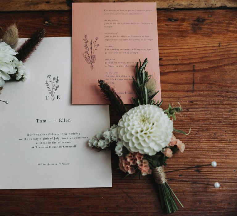 Simple wedding stationery complete in white and coral on a wooden table next to florals