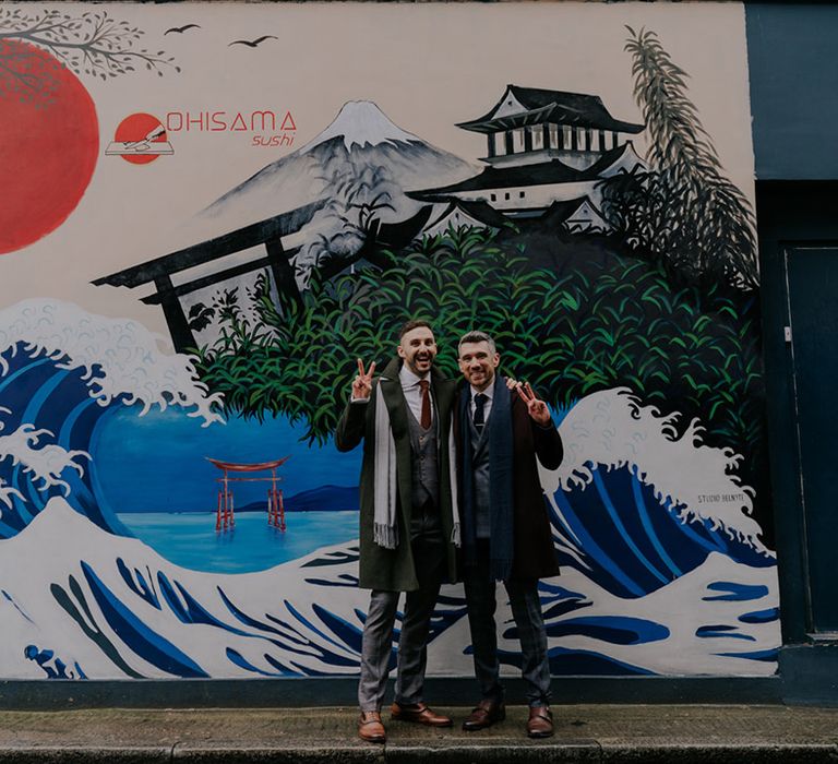 Grooms stand in front of brightly painted wall mural for their wedding day in London