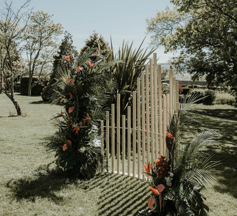 White wooden posts with tropical floral installation either side in landscaped grounds for birds of paradise wedding inspiration