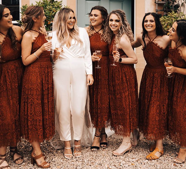 Bride stands with her bridesmaids who wear red dresses with lace and halter-necks 