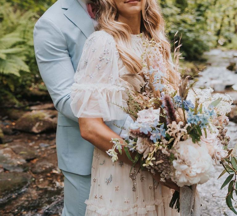 Bride leans back into groom as she holds her floral bouquet