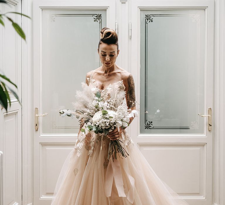 Tattooed bride holds her pampas grass floral bouquet whilst wearing boho chic romantic wedding gown