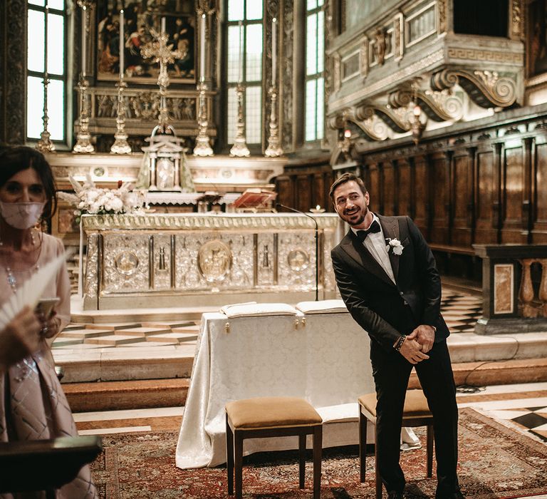 Groom wears black tie on his wedding day as he stands at the front of the aisle before wedding ceremony in church