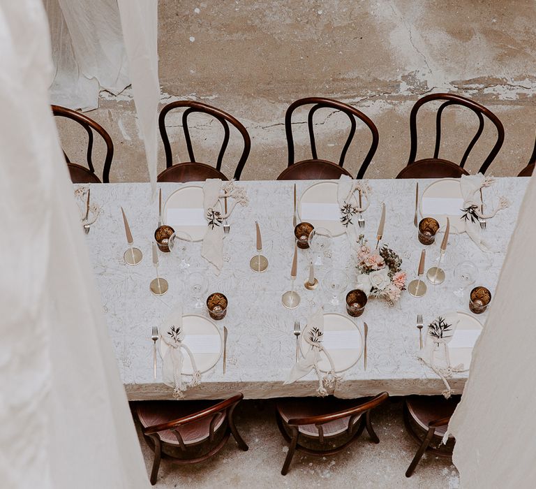 Birds eye view of the minimalist wedding table settings at Bylaugh Hall with patterned tablecloth neutral table ware, gold cutlery and taper candles 