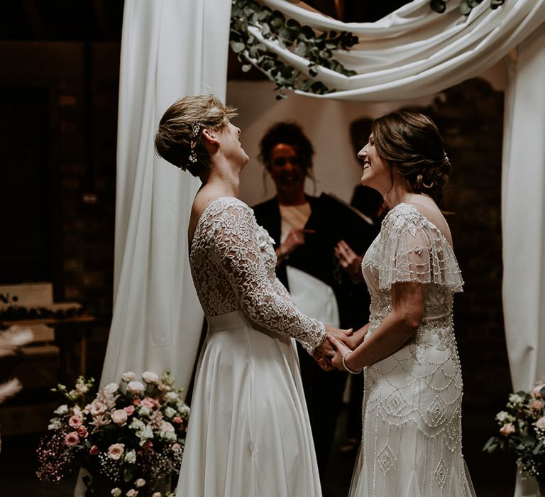 Same sex wedding ceremony with two brides in an appliqué and embellished gown holding hands laughing  