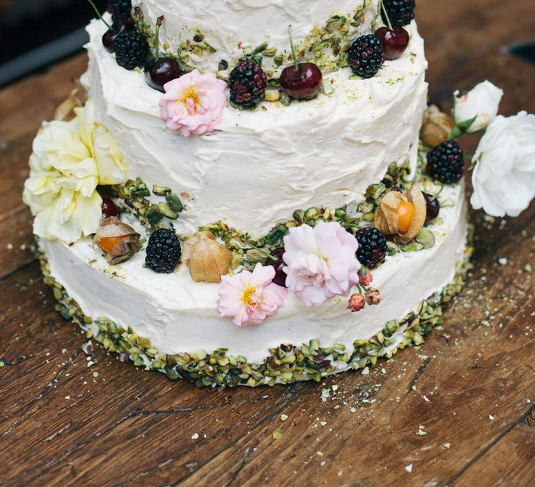 Two tier wedding cake decorated with fruit and an open pink peony flower head as the cake topper 