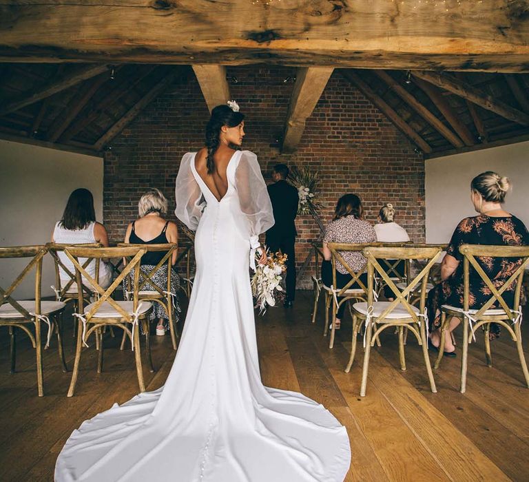 Bride in a fitted wedding dress with puddle train and puff sleeves waiting to walk down the altar at Brickhouse Vineyard