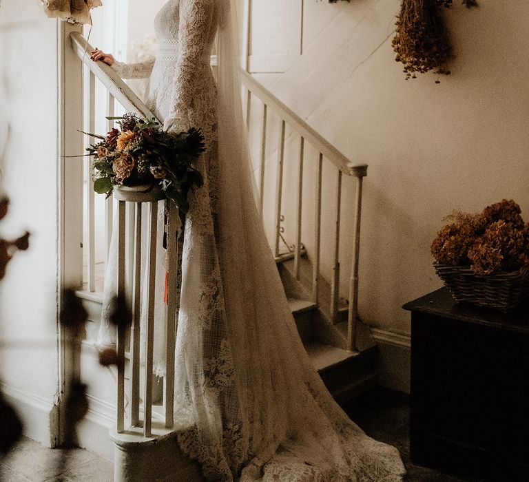 Bride in a lace wedding dress with plunging neckline and bell sleeves at Lyde Court wedding with hanging dried crops on the wall 