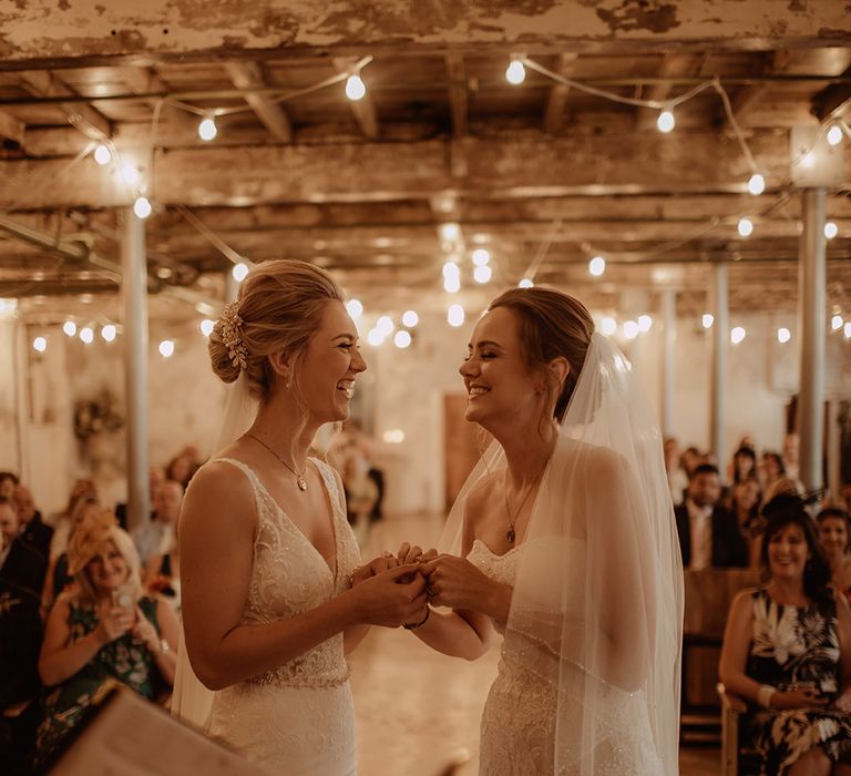 Brides hold hands and look lovingly at one another during wedding ceremony