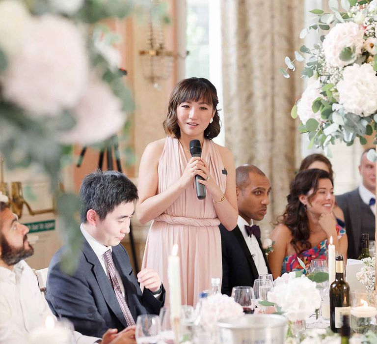 Bridesmaid wearing blush pink gown gives speech during reception