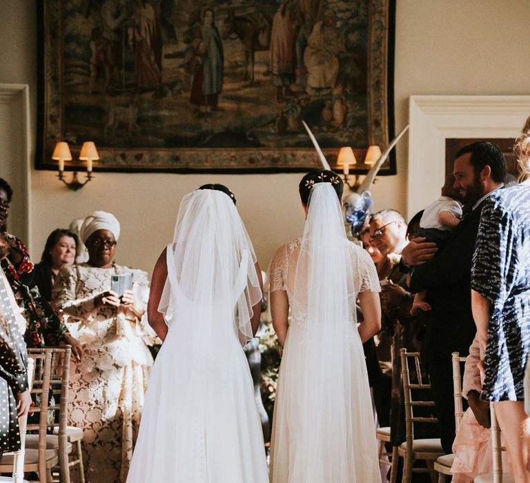 Two brides with long cathedral length veils walking down the aisle together at their Elmore Court wedding 