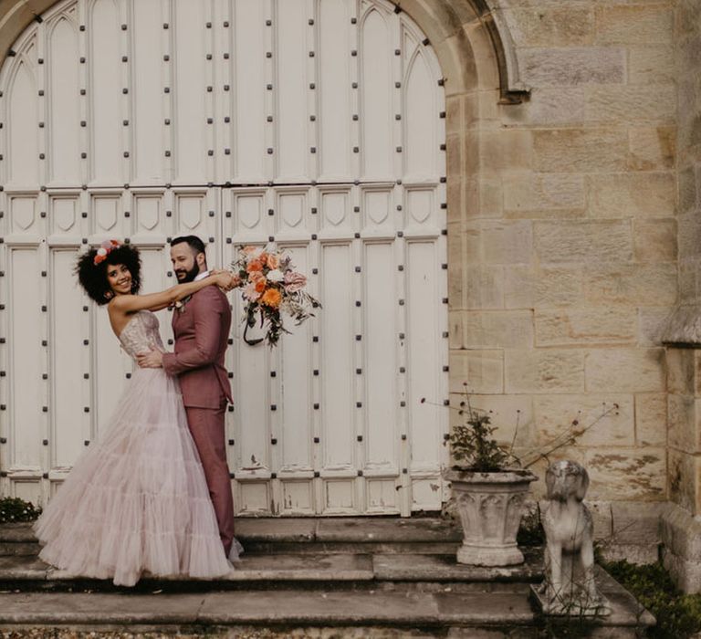 Groom in a pink suit embracing his bride in pink bridal separates with full tulle skirt and strapless corset top 