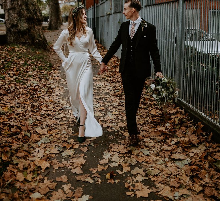 Bride & groom walk with one another whilst holding hands on their wedding day