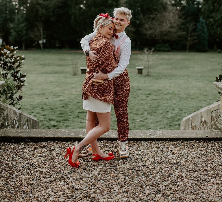 LGBTQ+ wedding with bride in a leopard bring suit embracing her bride in a short wedding dress with red bow shoes 