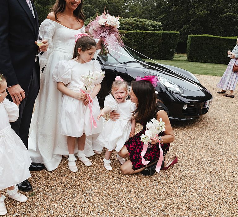 Young bridesmaids stand together with bride and other guests as one of them starts to cry