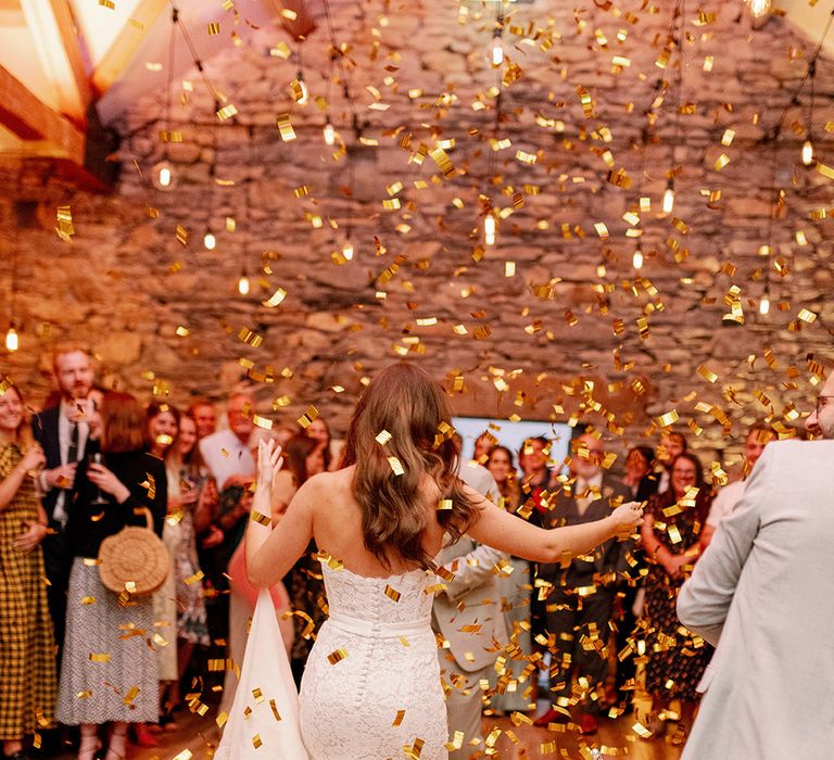 Bride and groom walk onto the dancefloor with na explosion of gold confetti