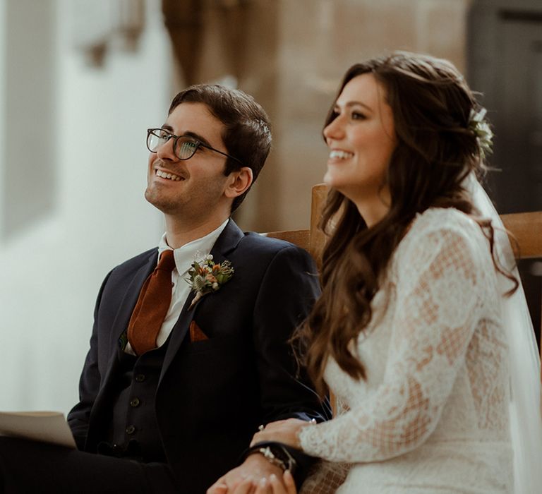 Bride in lace Maggie Sottero wedding dress sits next to groom in blue suit for church wedding ceremony 