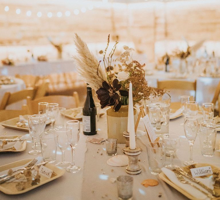 Table setting with small flower centrepiece, white candles, wooden plates and gold cutlery