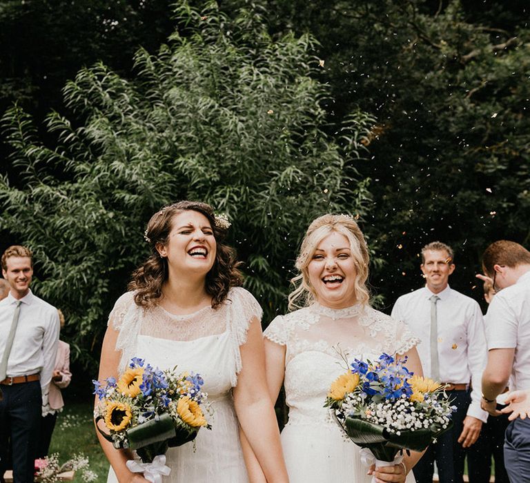 Yellow, purple and white bouquets for brides having their confetti exit from ceremony