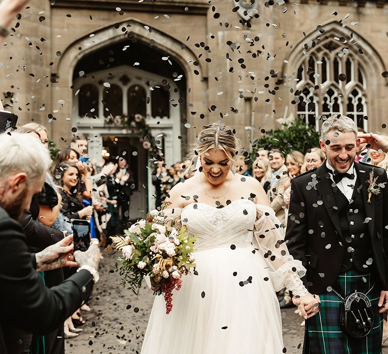 Bride and groom walk past all their wedding guests as they throw black confetti for the couple outside Drumtochty Castle 