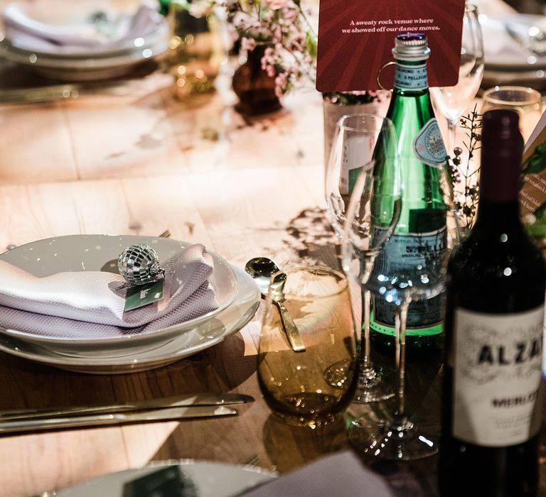 White plates with lilac napkins and name place cards with disco ball charm with red and white table name sign named after special places to the couple