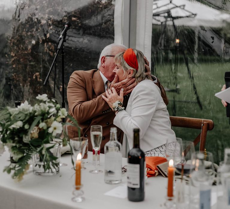 Father and mother of the groom kissing during the clear glass marquee reception 