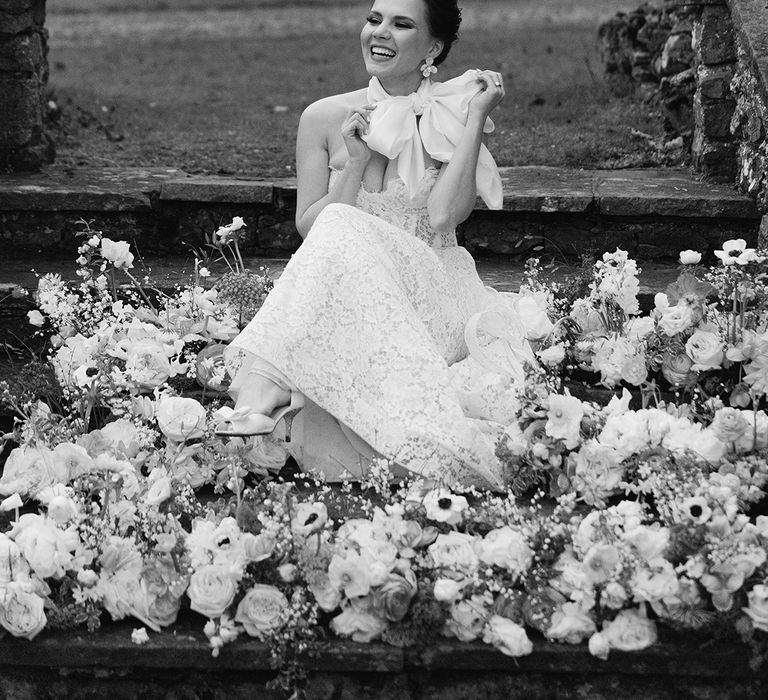 black and white portrait of the bride in a strapless lace wedding dress and satin neck scarf sitting on the steps at Holesfoot