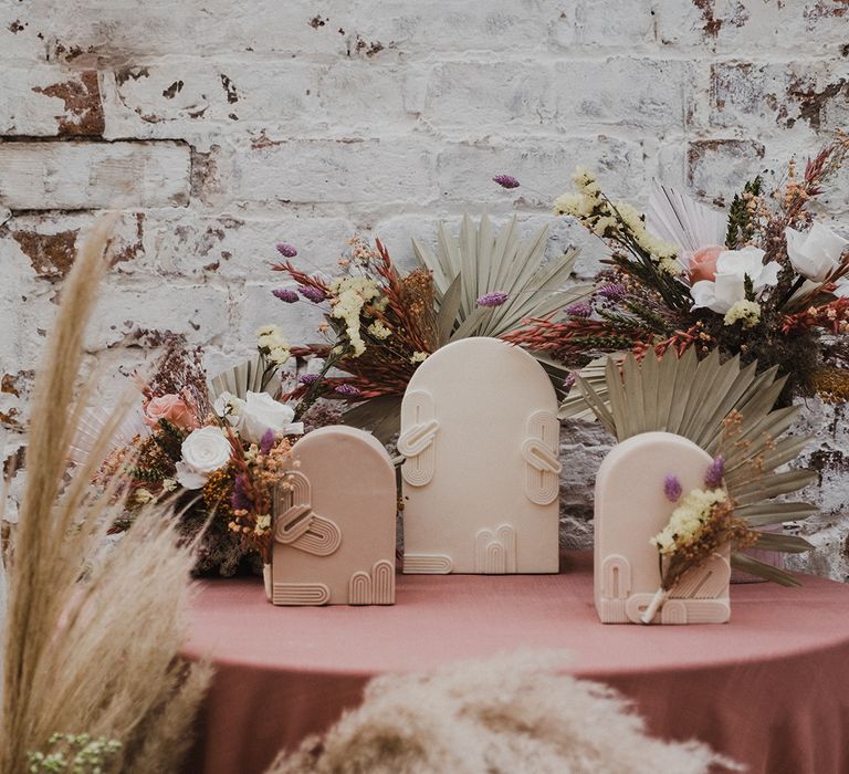 wedding cake table with varying size wedding cakes surrounded by pastel flowers and grasses 