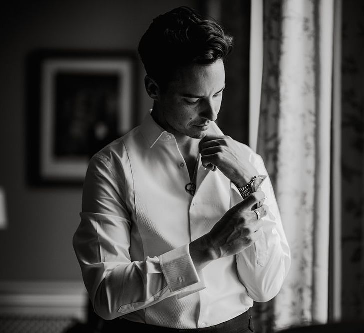 Black & white image of groom doing up his cufflinks and wearing white shirt on the morning of his wedding day