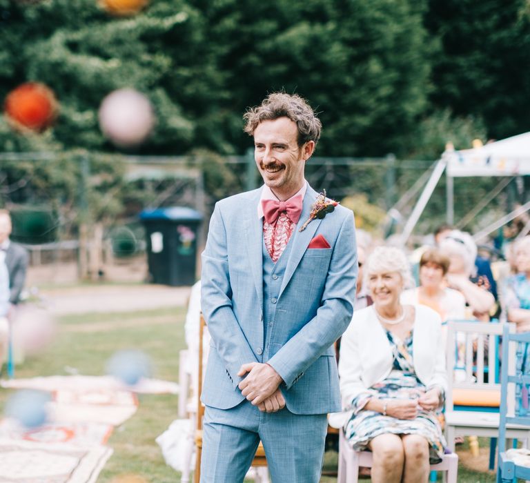 Groom wears dusty blue suit and link ruffled 70s shirt with pink bow-tie 