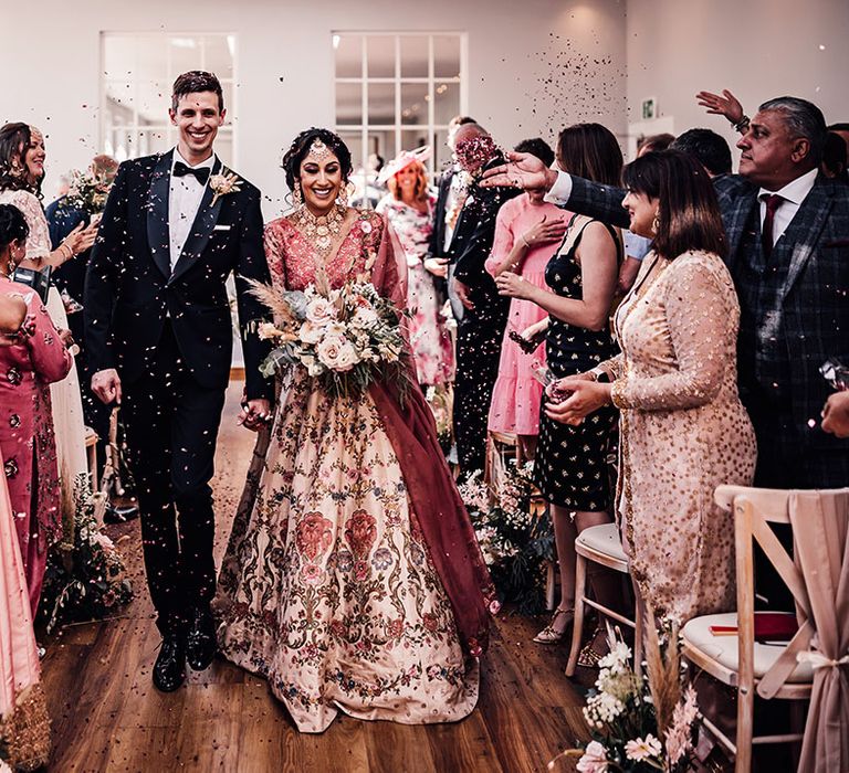 Bride & groom walk through colourful confetti after wedding ceremony at Bredenbury Court Barns