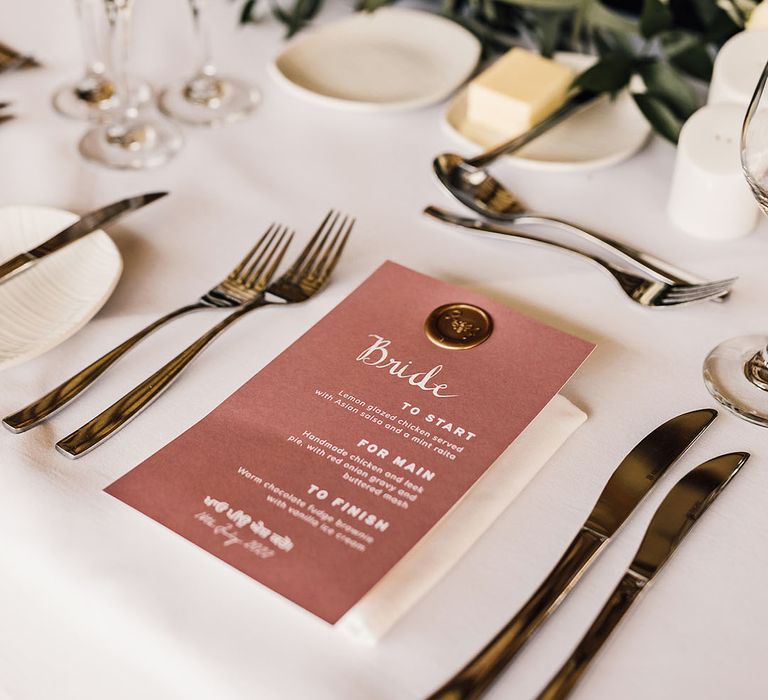 Wedding stationery menu complete with gold personalised wax stamp on white tablecloth with neutral styled floral arrangements 