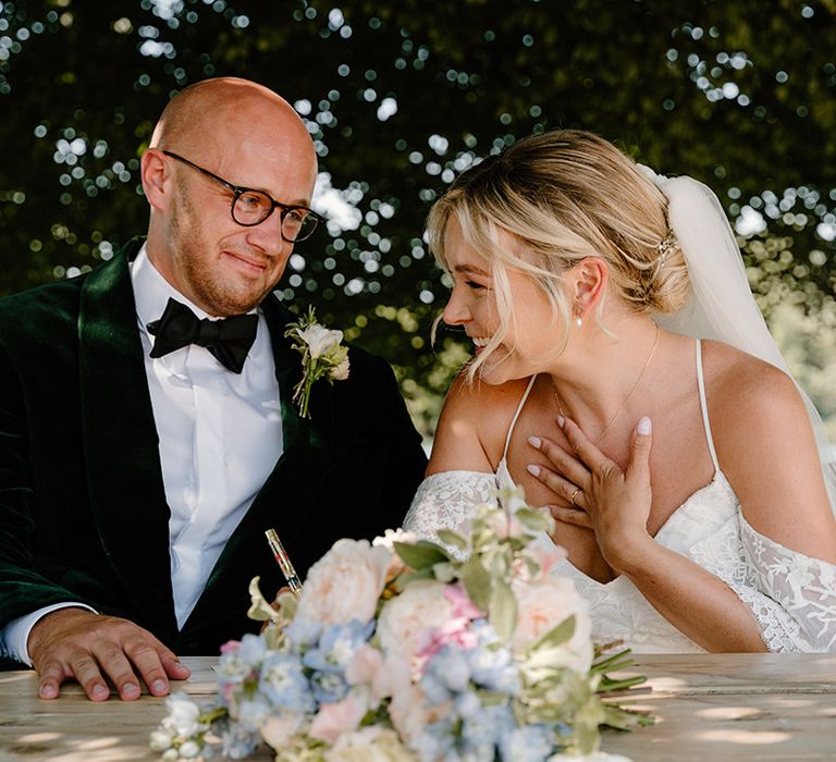 Bride & groom sign marriage certificate as they sit beside the bank of the River Thames