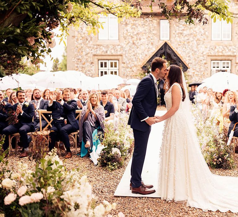 Bride and groom share their first kiss as a married couple with guests clapping 