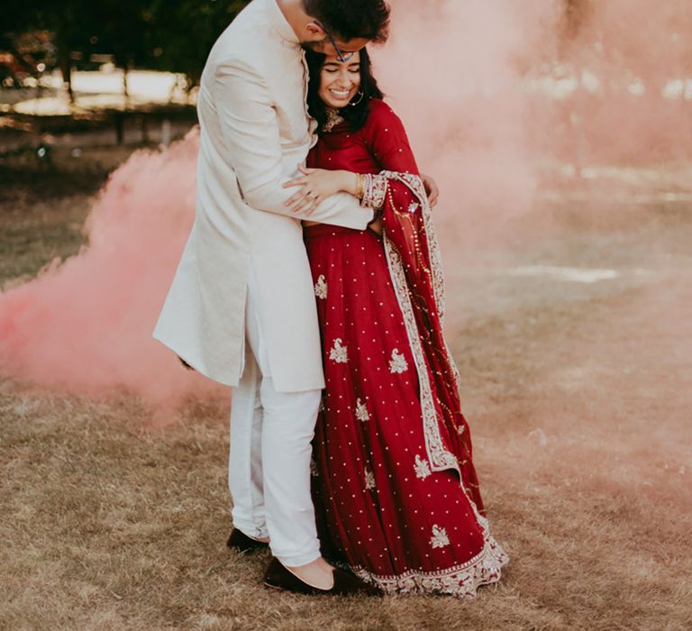 Bride & groom kiss in front of orange smoke bomb outdoors 