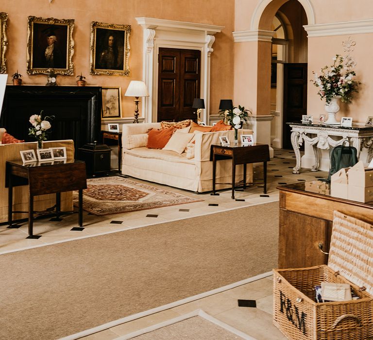 Orangey pink room at Kelmarsh Hall with large alternative glass chandelier, framed portraits, burnt orange pillows, a grand piano and large floral displays in ceramic vases