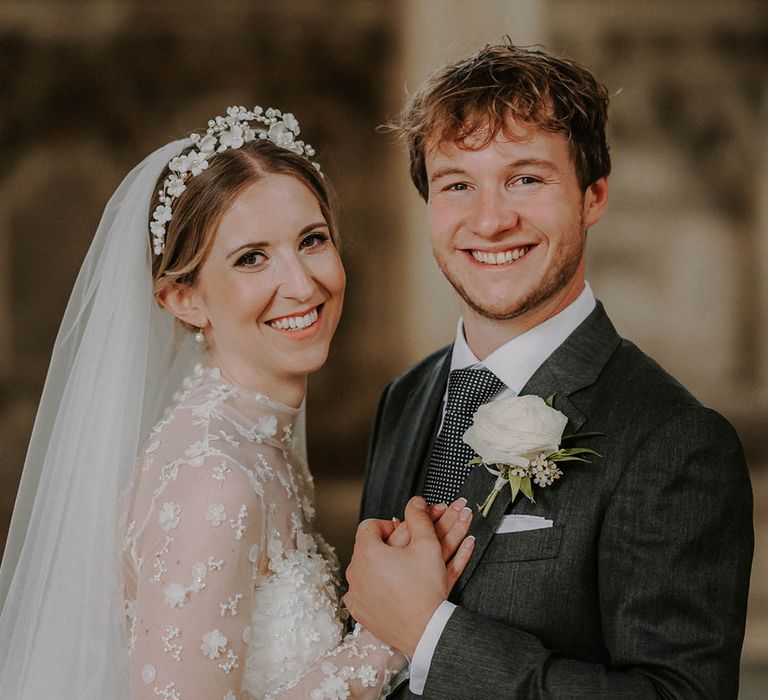 Groom in dark suit with dotted tie and white rose buttonhole with the bride in a high neck long sleeve wedding dress 