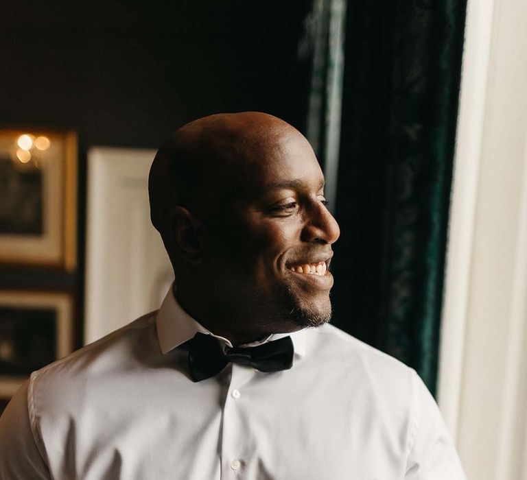 Groom in crisp white shirt and black bowtie smiling and getting ready at Pepper Arden Hall