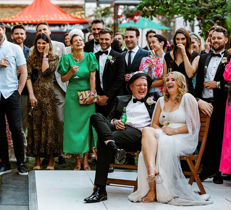 Bride & groom laugh during wedding speeches surrounded by family and friends 