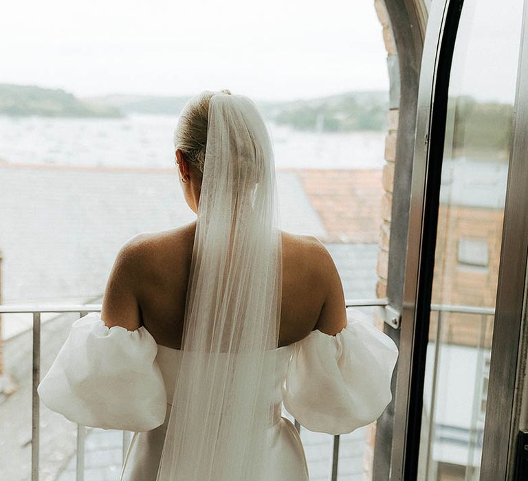 Bride wears floor-length veil and Jesus Peiro wedding dress as she looks out toward the sea