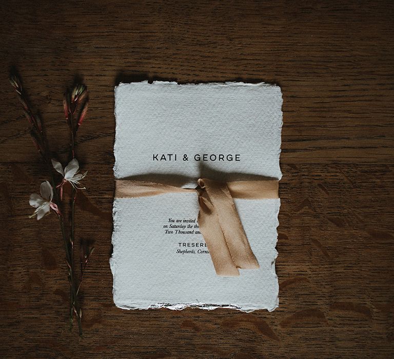 White classic wedding stationery tied with silk ribbon beside flowers 