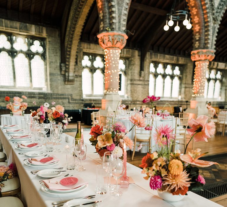 Fairy lights wrap around church pillars beside white round tables with colourful floral arrangements and bright pink Chinese inspired name cards