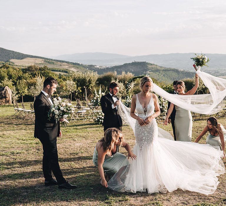 Brides veil blows in the wind beside her bridesmaids in pale green satin cowl neck bridesmaid dresses