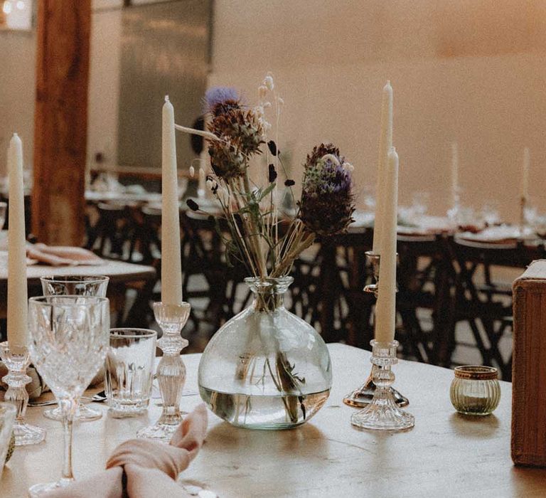 DIY wedding flower arrangements in glass vase beside white candles on wooden tables 