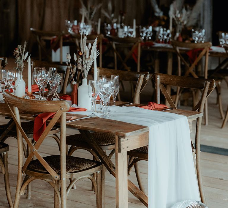 Rustic wooden table decorated with white table runners, burnt orange napkins and disco balls with bunny grass floral arrangements 