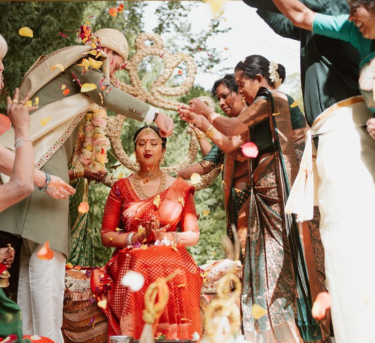 South Asian bride in a red legenga having petals sprinkled over her 