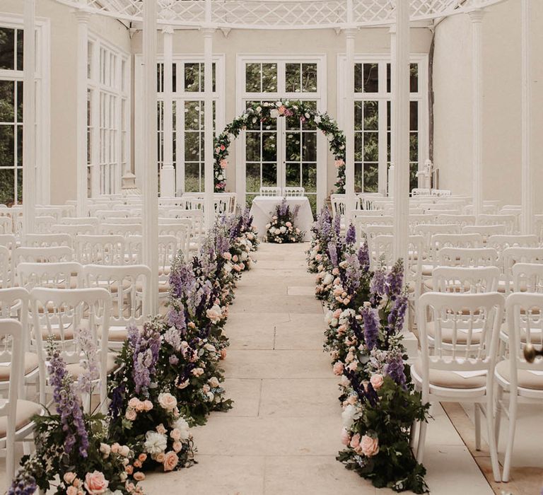 Purple stock, pink roses and white flowers with greenery make up the aisle and altar decoration for indoor wedding 