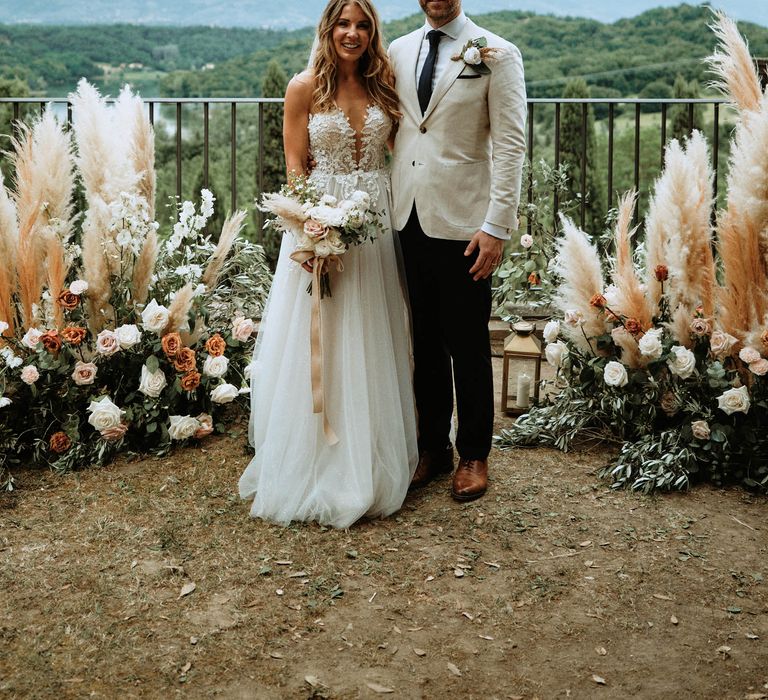 Bride and groom at altar with pampas grass, eucalyptus and white, orange and pink rose decor.