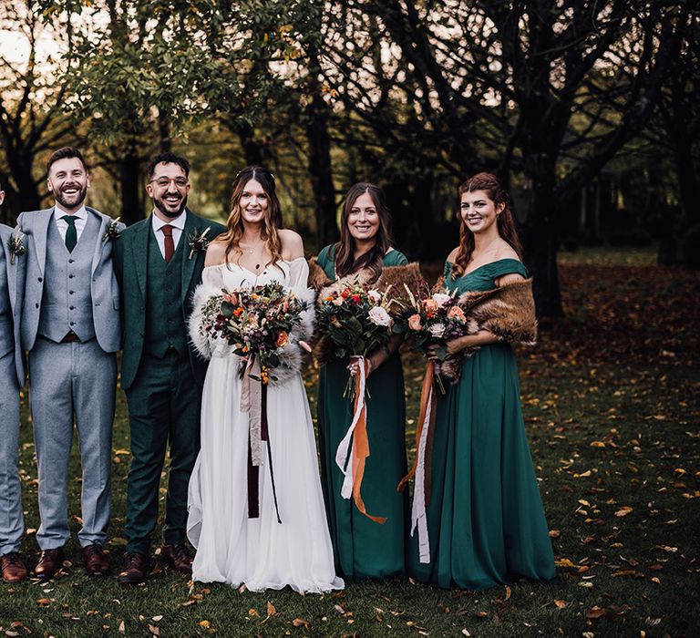 Forest green autumnal bridesmaid dresses with winter shawl standing with the groomsmen in light grey three piece suit with green ties 