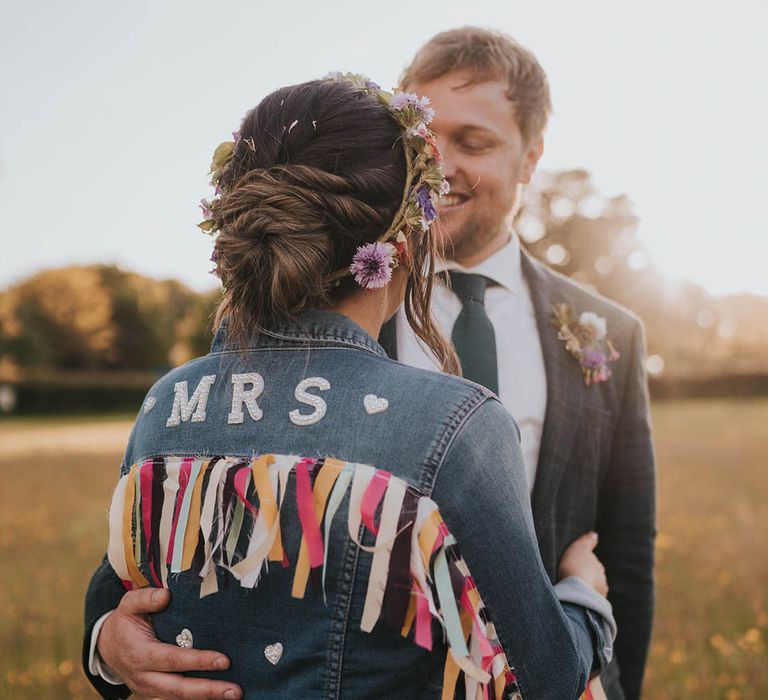 Bride wearing flower crown and dark blue denim jacket with pearl name on the back of the jacket and colourful tassels 